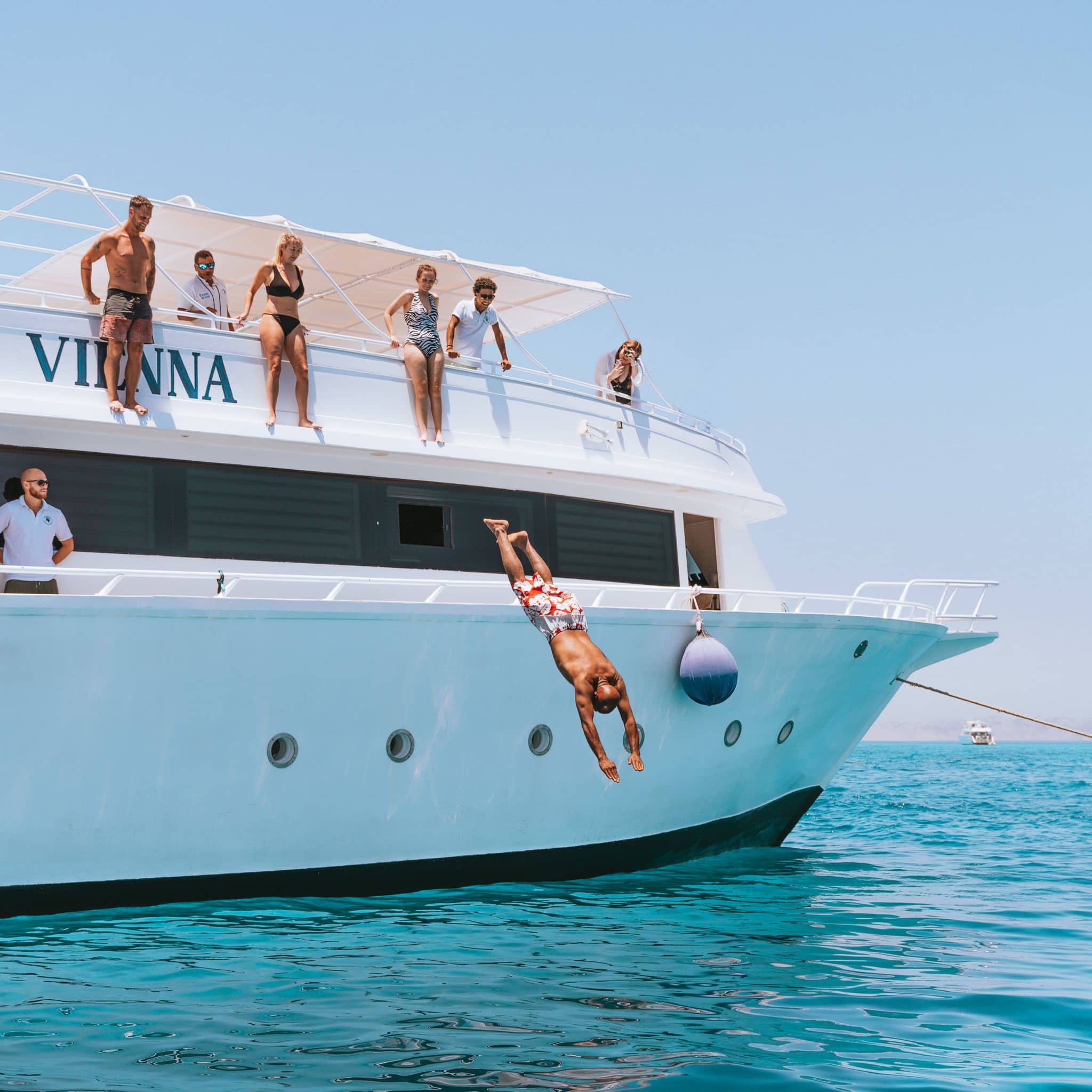Person diving headfirst from a white yacht named VIANNA into clear turquoise water.