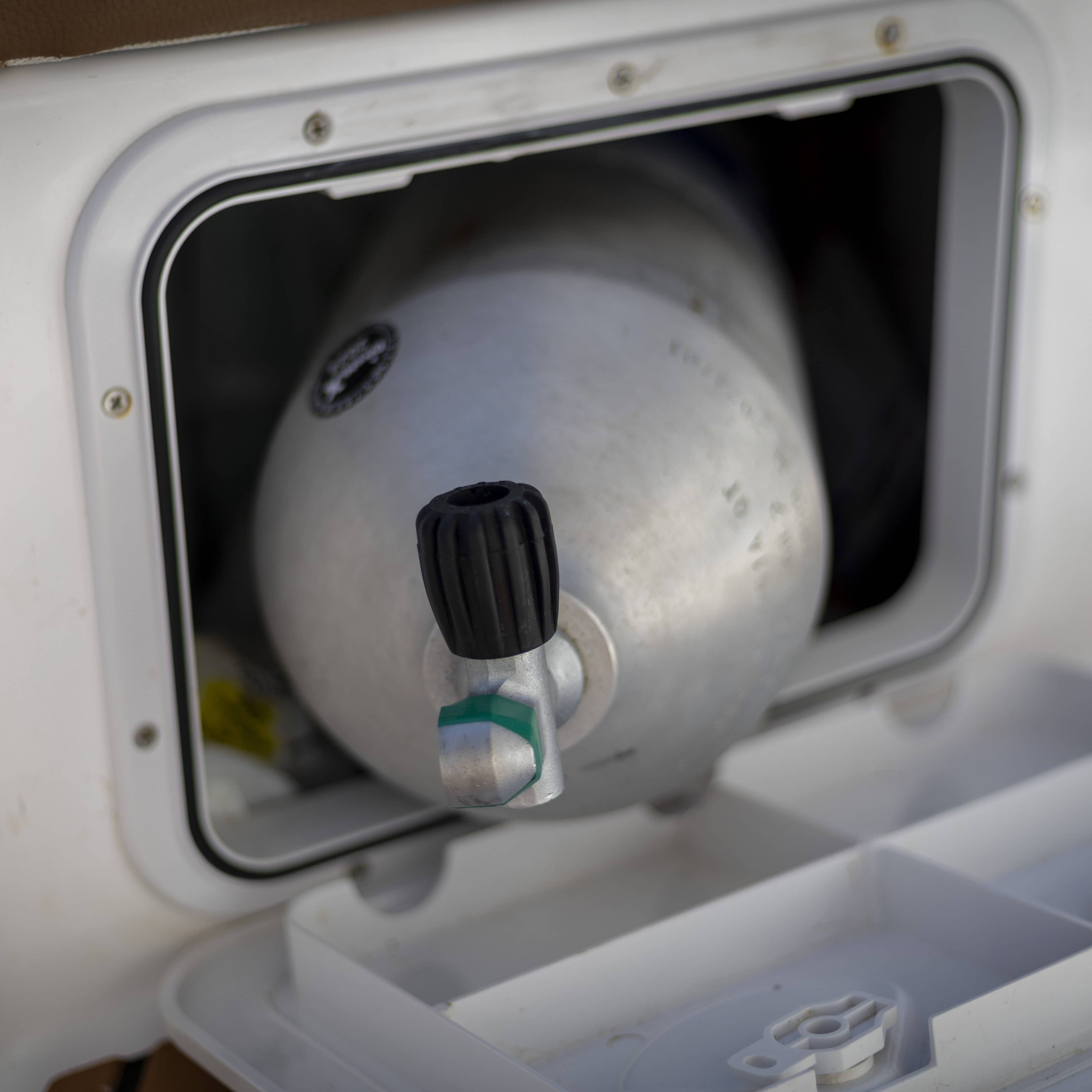 A gray scuba tank stored neatly inside a white compartment on a boat.