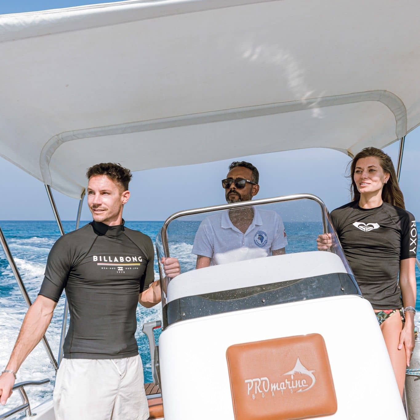 Three people enjoy a sunny day on a boat, one steering through blue ocean.