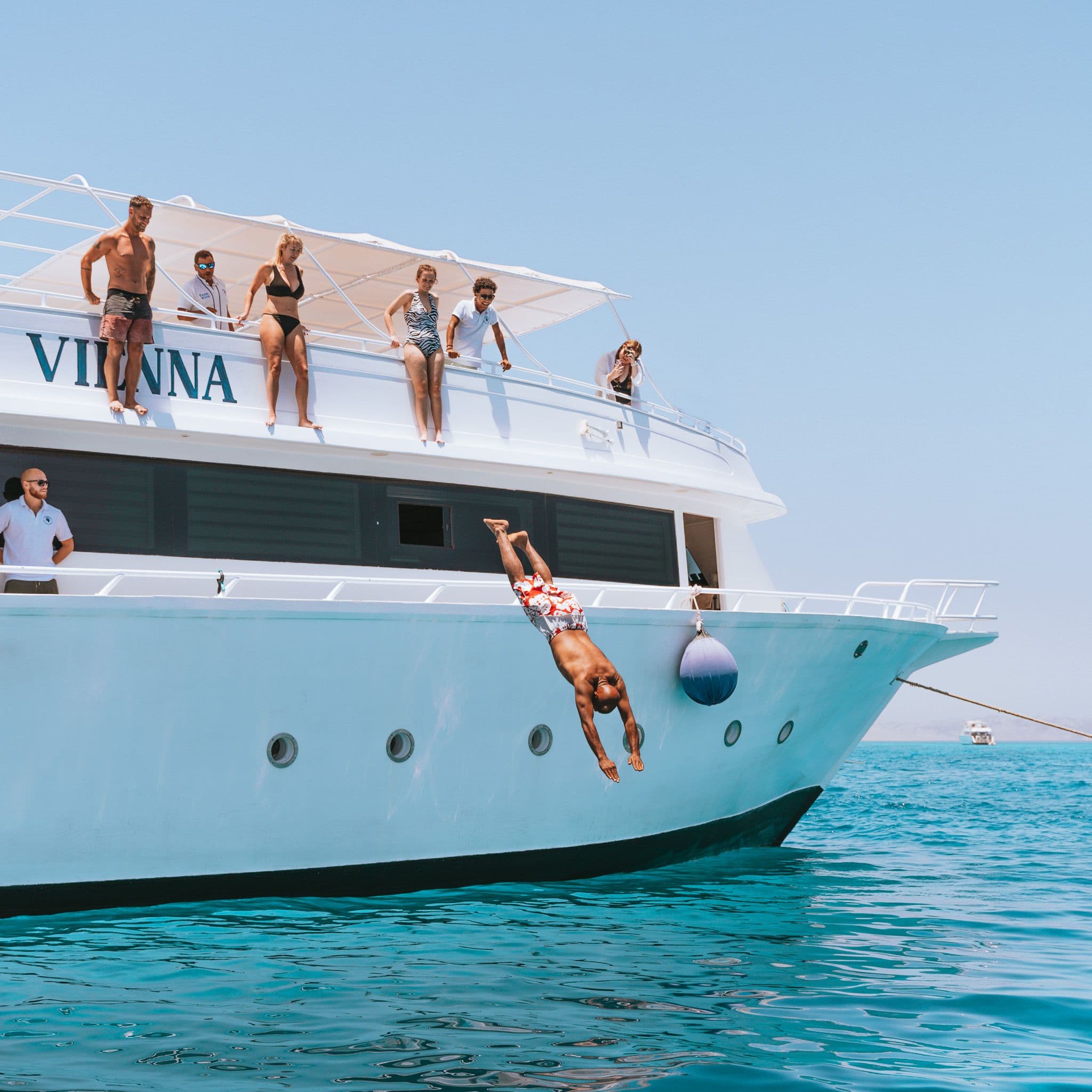 People on the top deck of a boat, one person diving into the ocean.
