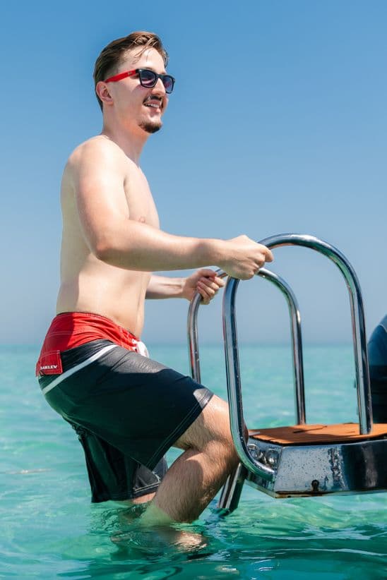 Man climbing a boat ladder from turquoise Red Sea water