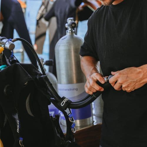 A person connecting a hose to scuba diving equipment on a boat deck.