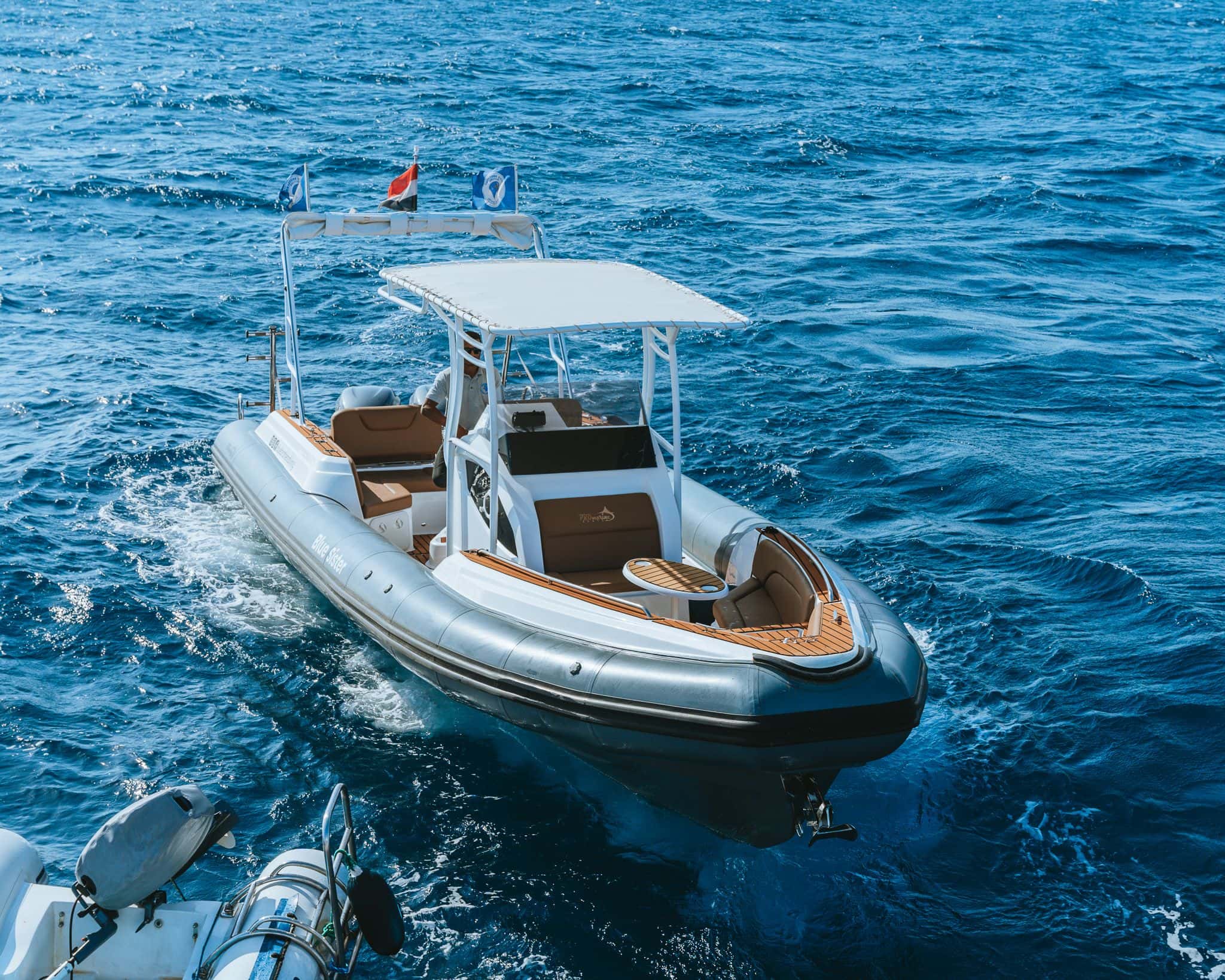 A sleek, grey rigid inflatable boat (RIB) with a white awning sailing on calm blue water.